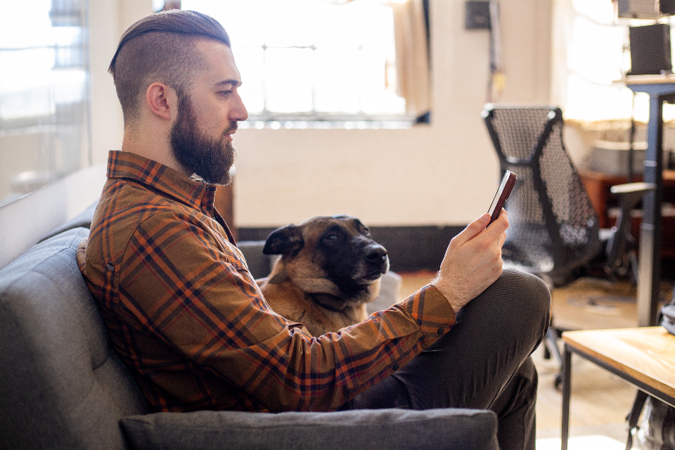 A man scrolling his phone with his dog asleep on his lap